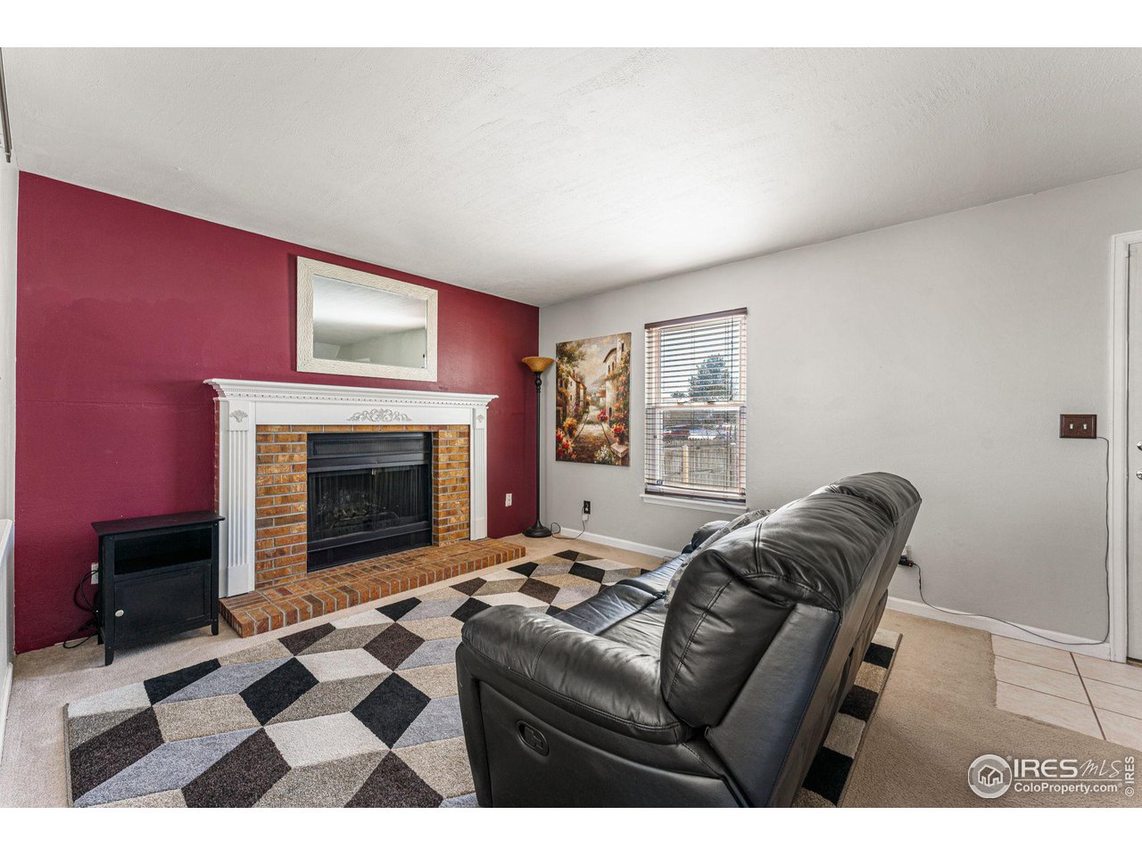 Living room with a brick fireplace, burgundy accent wall, and black leather reclining sofa.