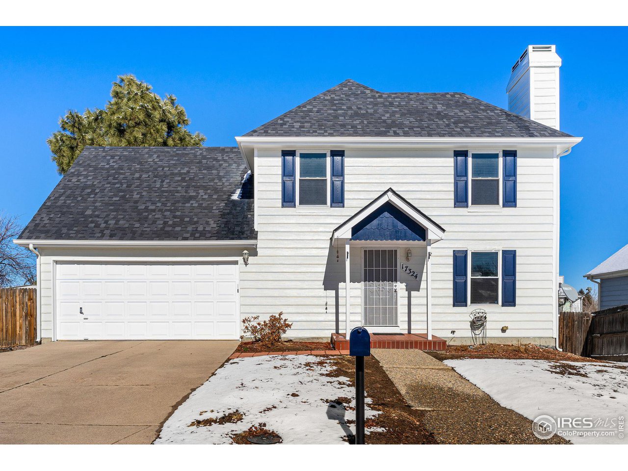 Two-story white house with blue shutters, a double garage, and snow patches in the front yard.