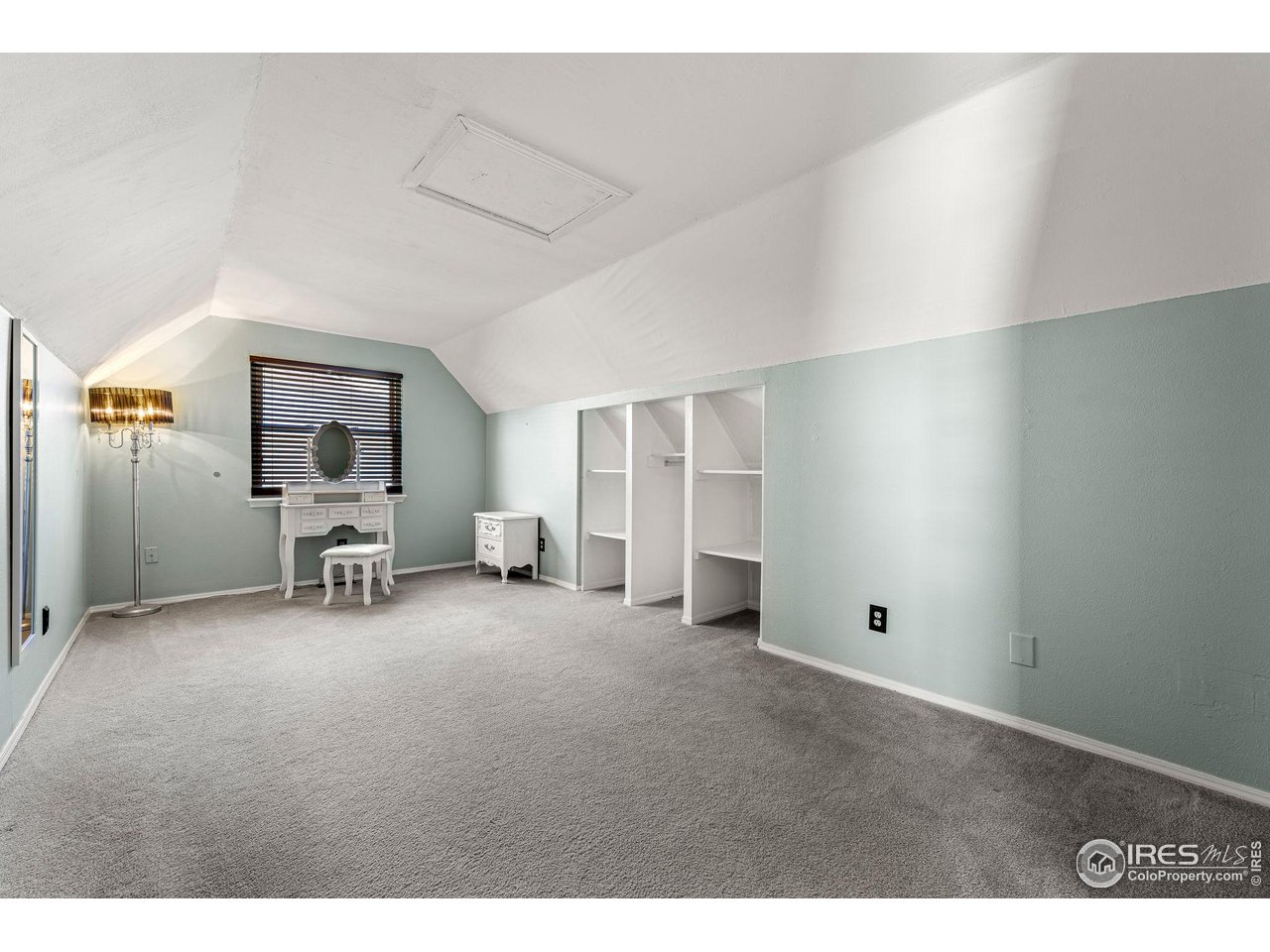 Attic bedroom with sloped ceilings, built-in shelving, and a vanity beneath a window.