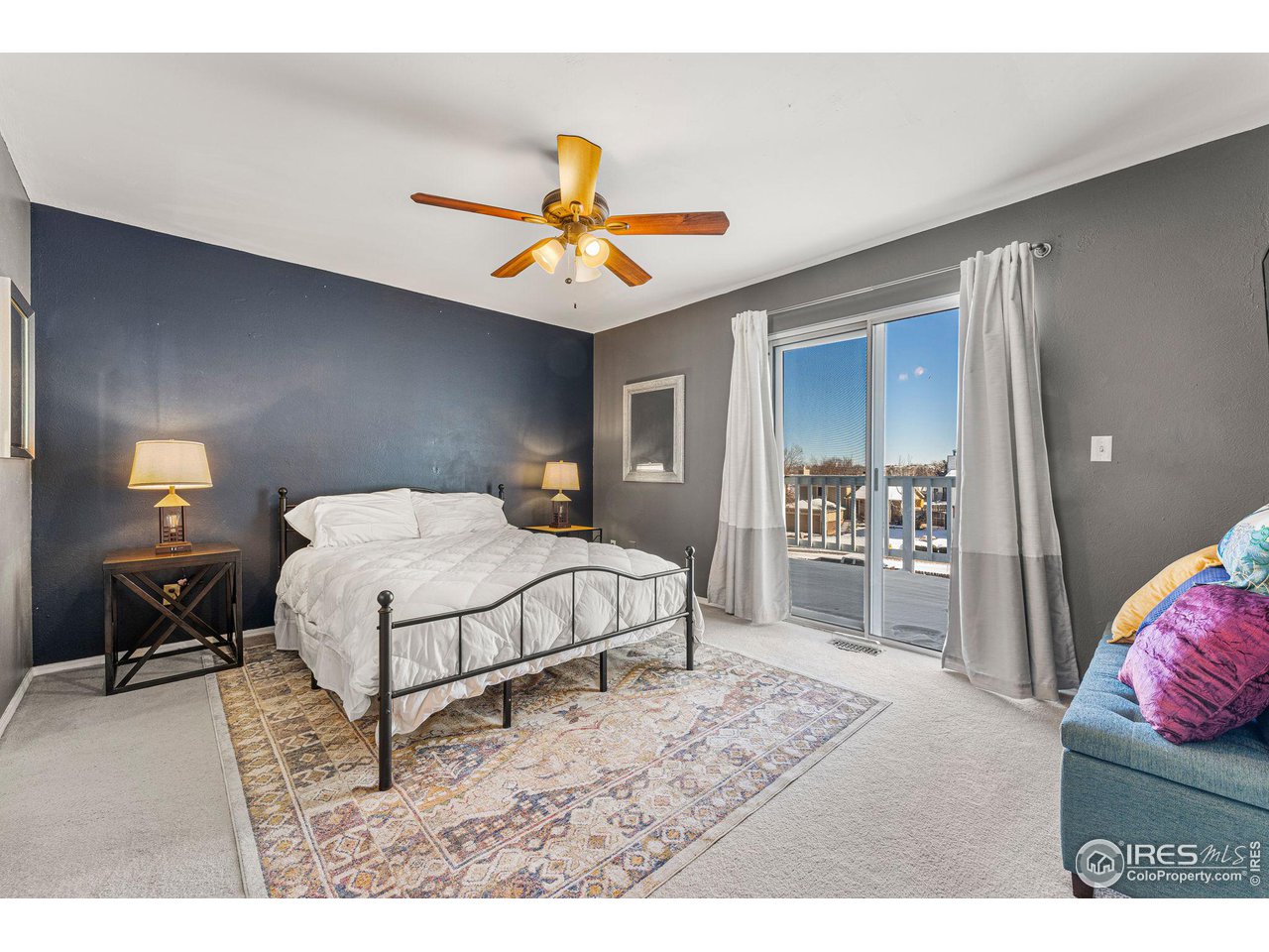 Bedroom with a black metal bed, patterned rug, ceiling fan, and sliding glass door to a balcony.