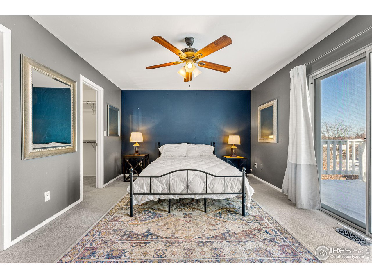 Bedroom with a dark blue accent wall, white bedding, patterned rug, and sliding glass doors to a deck.