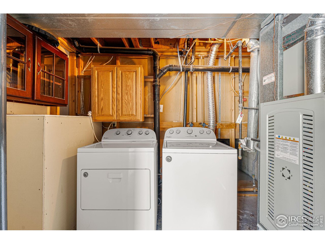 Laundry room with washer and dryer beneath wood cabinets beside the home's furnace.