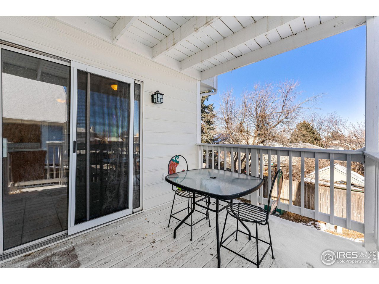 Covered balcony with a glass-top patio table and chairs overlooking leafless trees.
