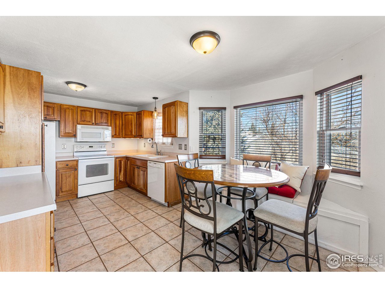 Kitchen and dining nook with wood cabinets, tiled floors, and large windows.