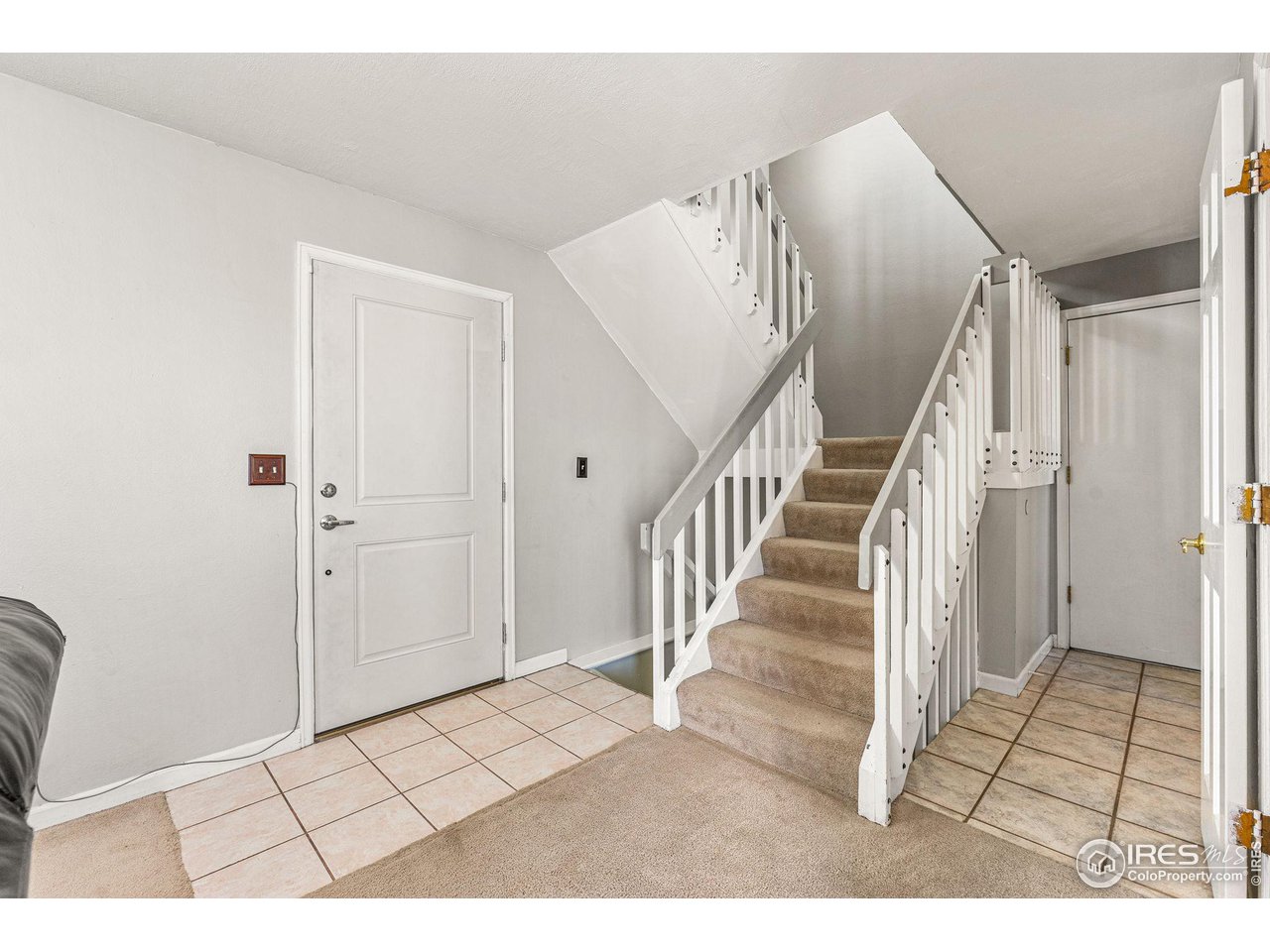 Entry hall with a carpeted staircase, white railings, and tiled flooring.