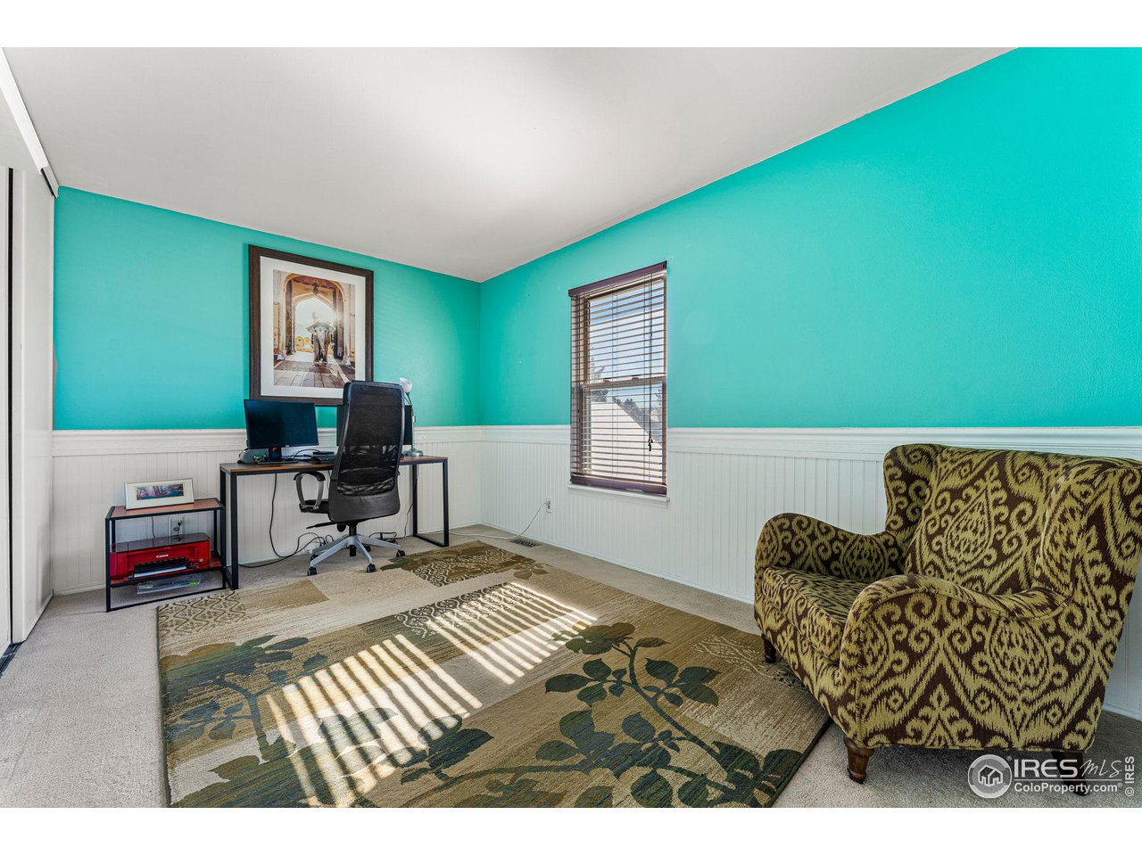 Home office with turquoise walls, white wainscoting, a desk, and a patterned armchair.