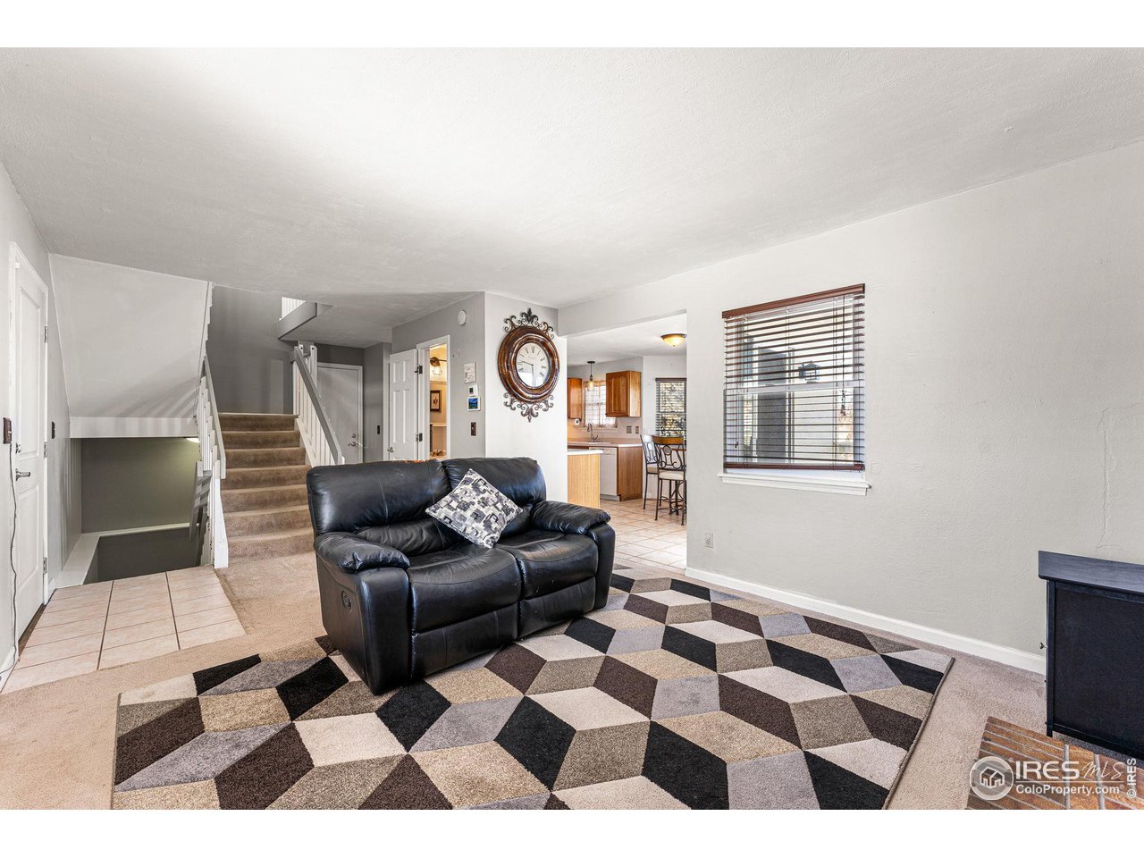 Living room with black leather loveseat, geometric rug, and open view to kitchen and staircase.