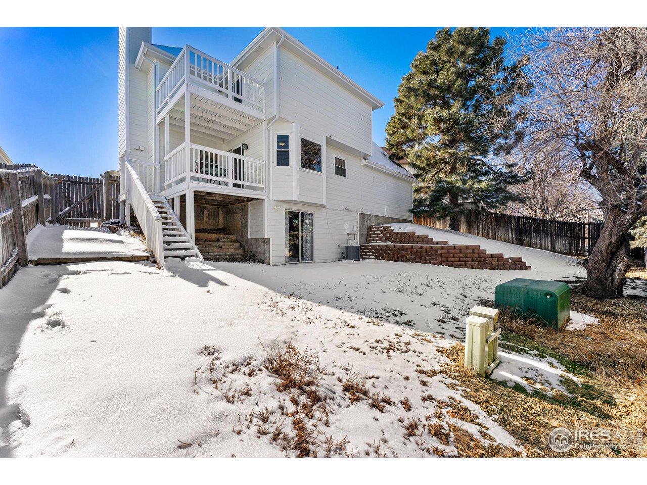 White two-story home with stacked rear balconies and stairs above a snow-covered fenced yard.