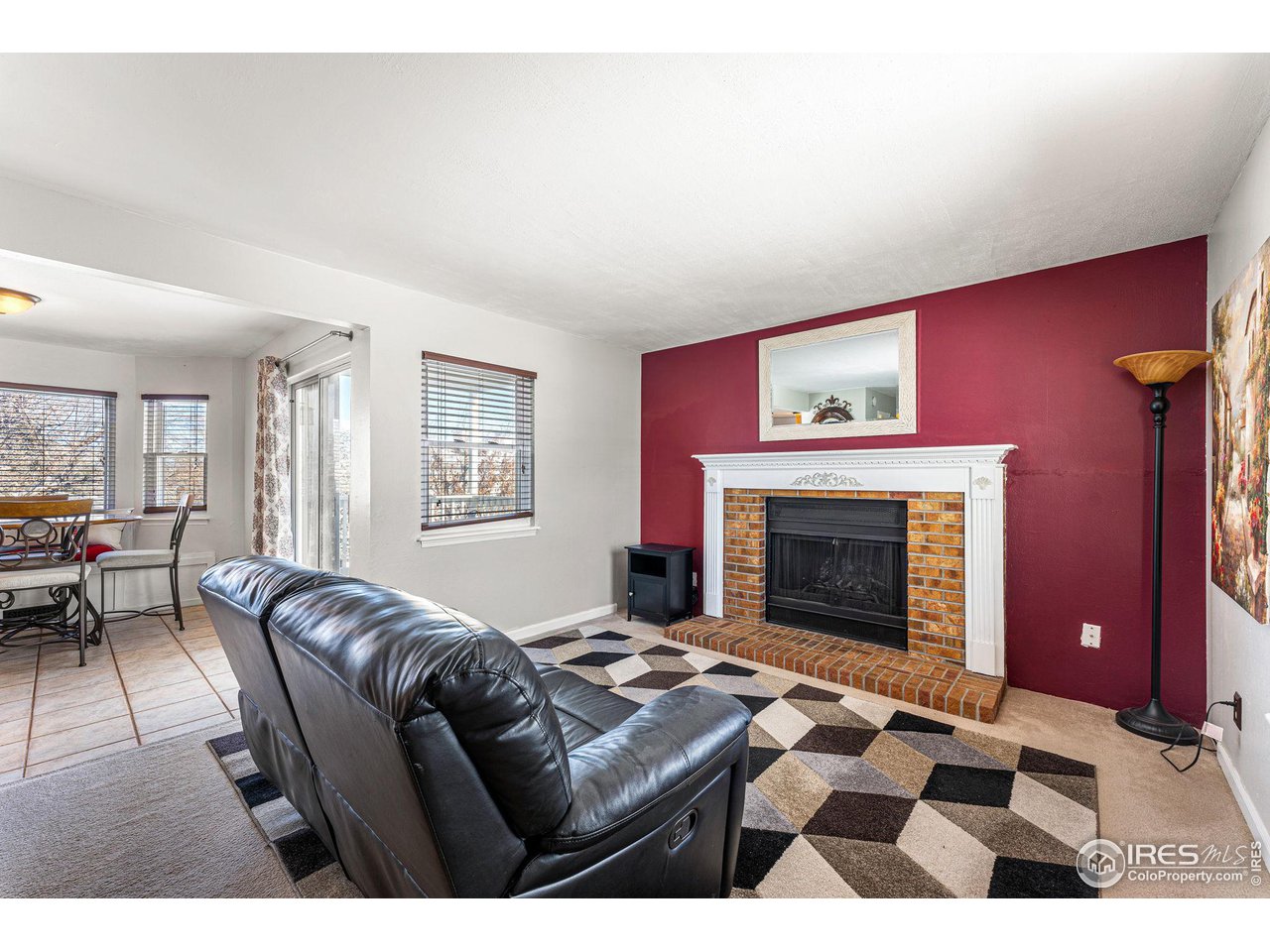 Furnished living room with a brick fireplace, burgundy accent wall, and black leather sectional.