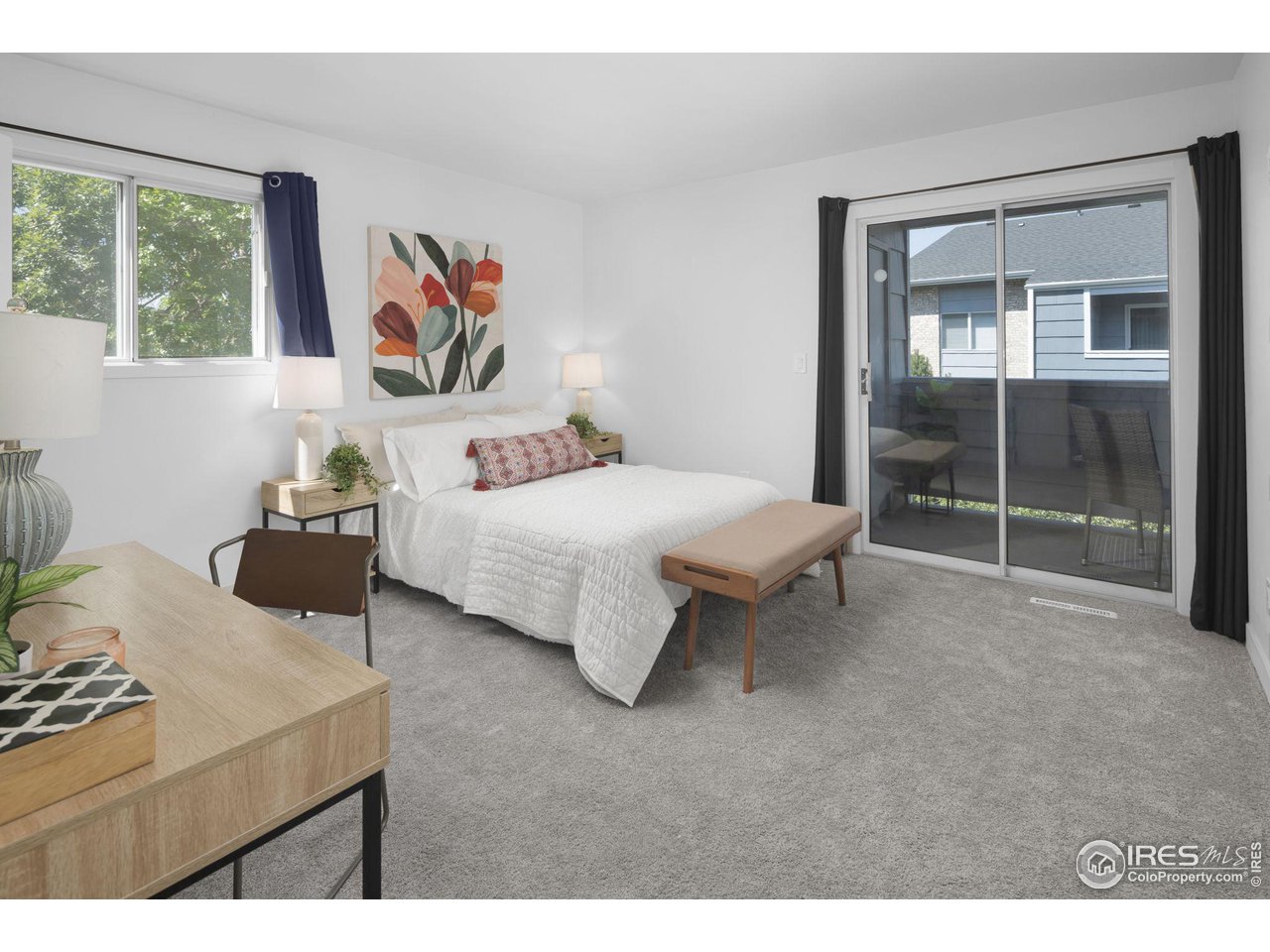 Staged bedroom with a white bed, floral wall art, and sliding glass doors to a balcony.