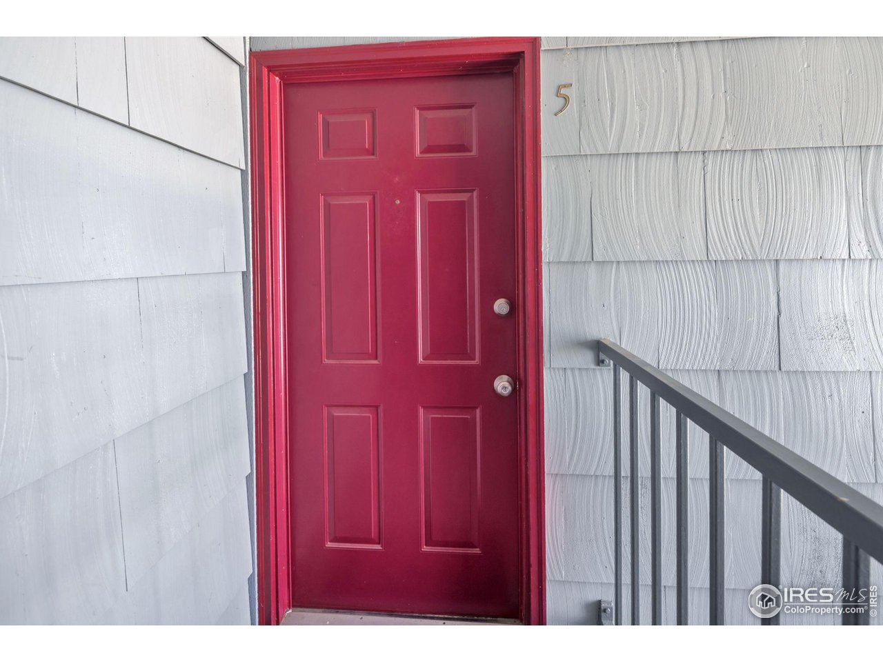 Unit 5’s red paneled front door against light gray shingle siding.