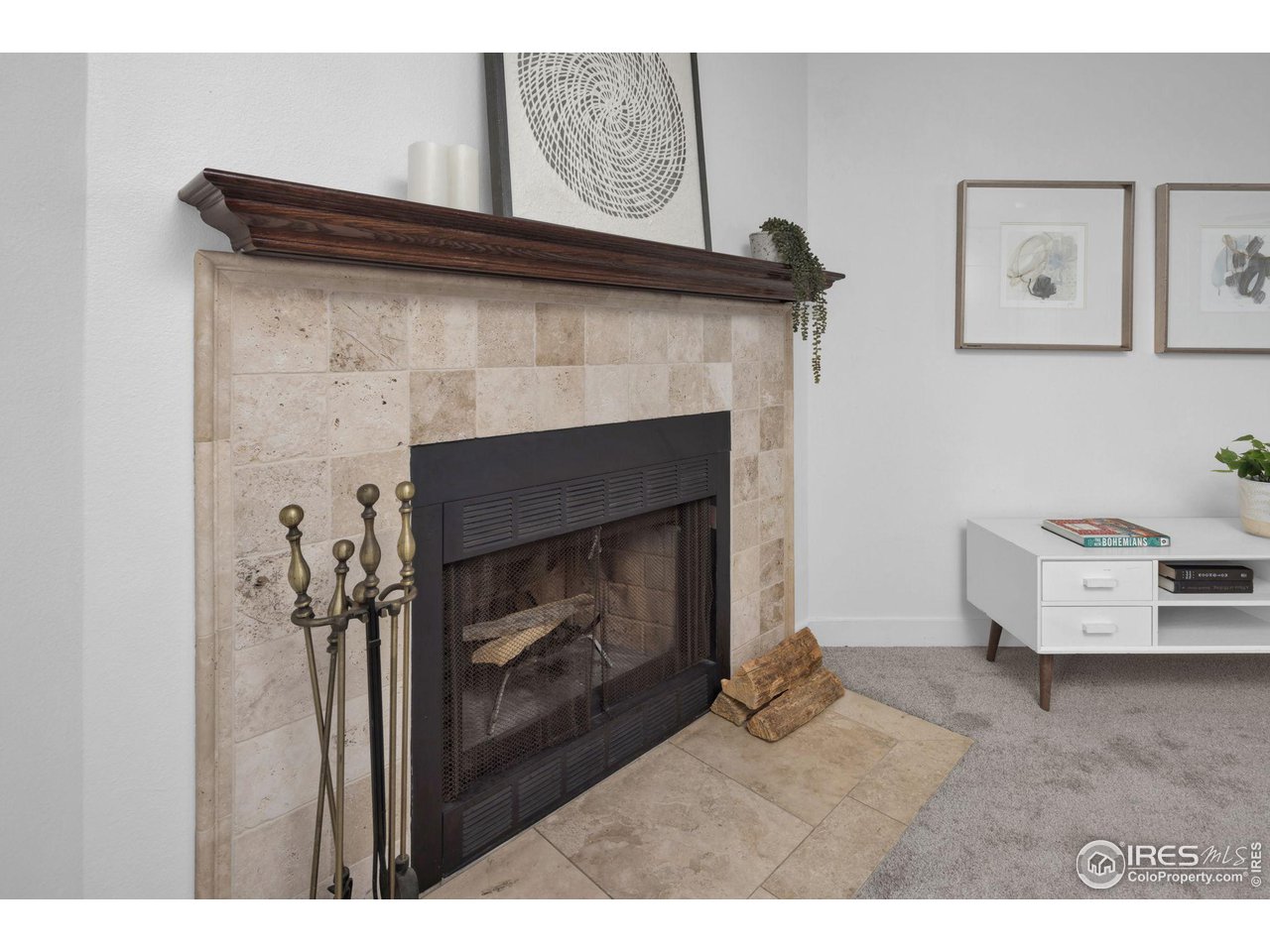 Living room fireplace with a beige stone surround, dark wood mantel, and brass fireplace tools.
