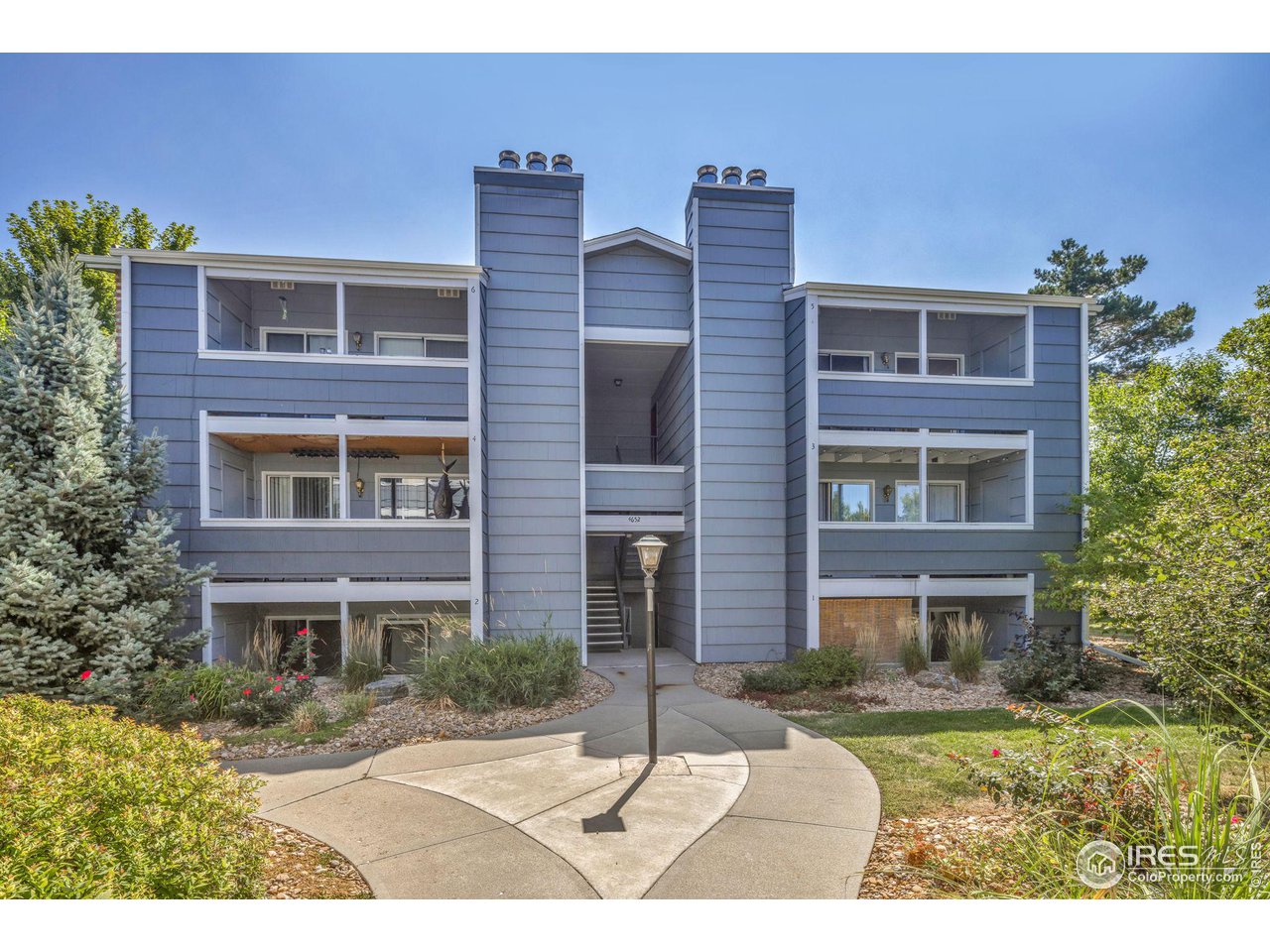 Blue-gray residential building with balconies, a central entrance, and curved walkway.