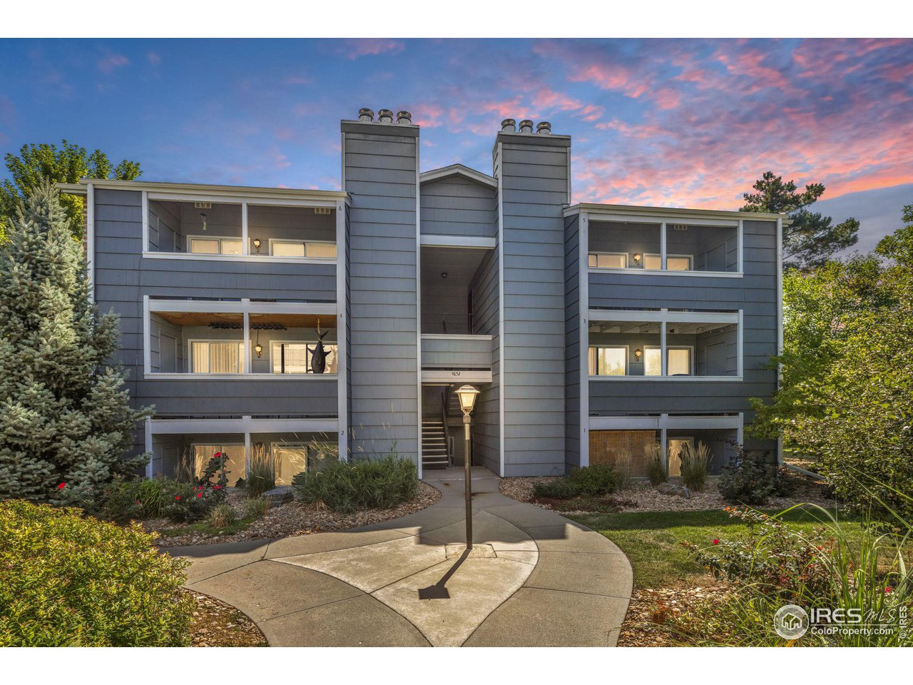 Gray multi-level condominium with balconies and a curved walkway under a pink evening sky.