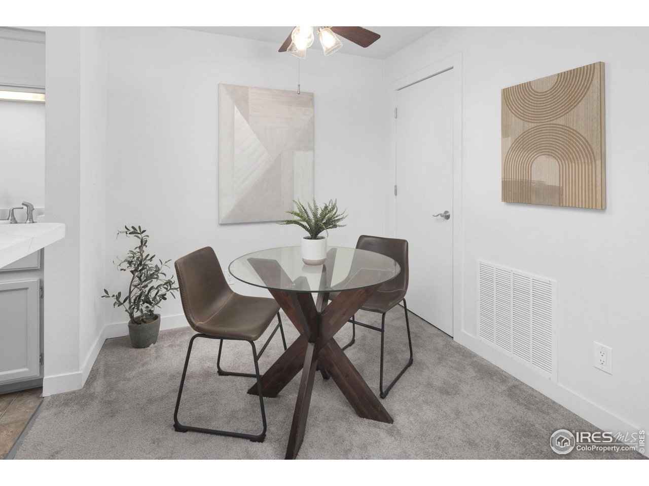 Dining area with a glass-top table, brown chairs, potted plants, and geometric wall art.