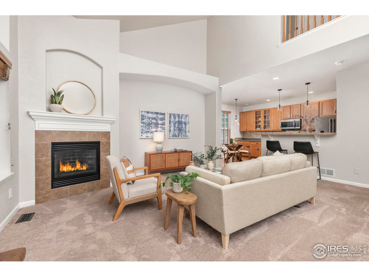 Living room with a tiled fireplace, vaulted ceiling, and open kitchen with wood cabinets.