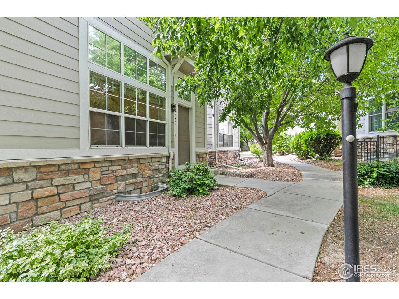 Townhouse entrance beside a landscaped walkway, shaded by leafy trees and marked by a black lamp post.