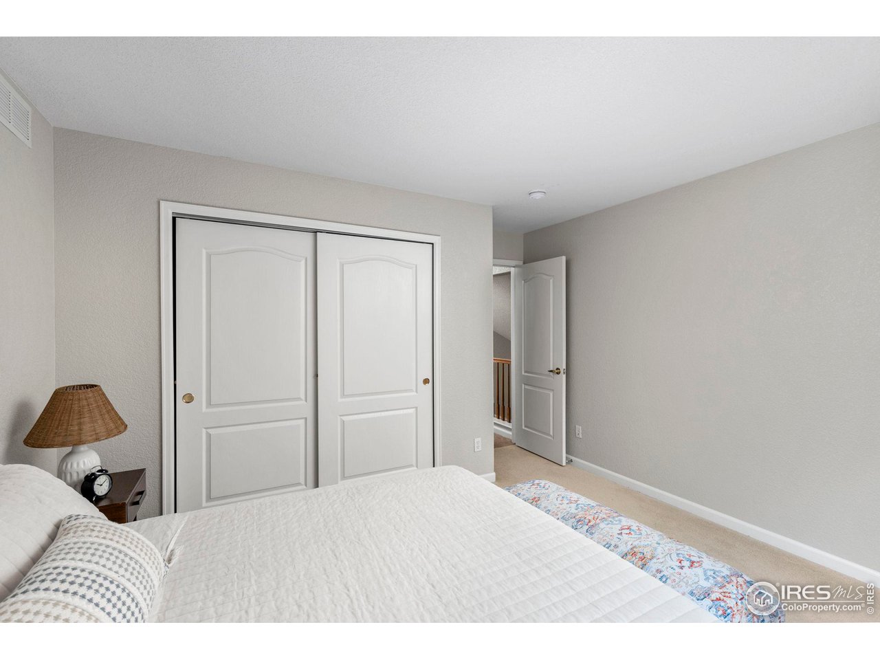 Bedroom with a white quilted bed, sliding closet doors, and an open doorway.