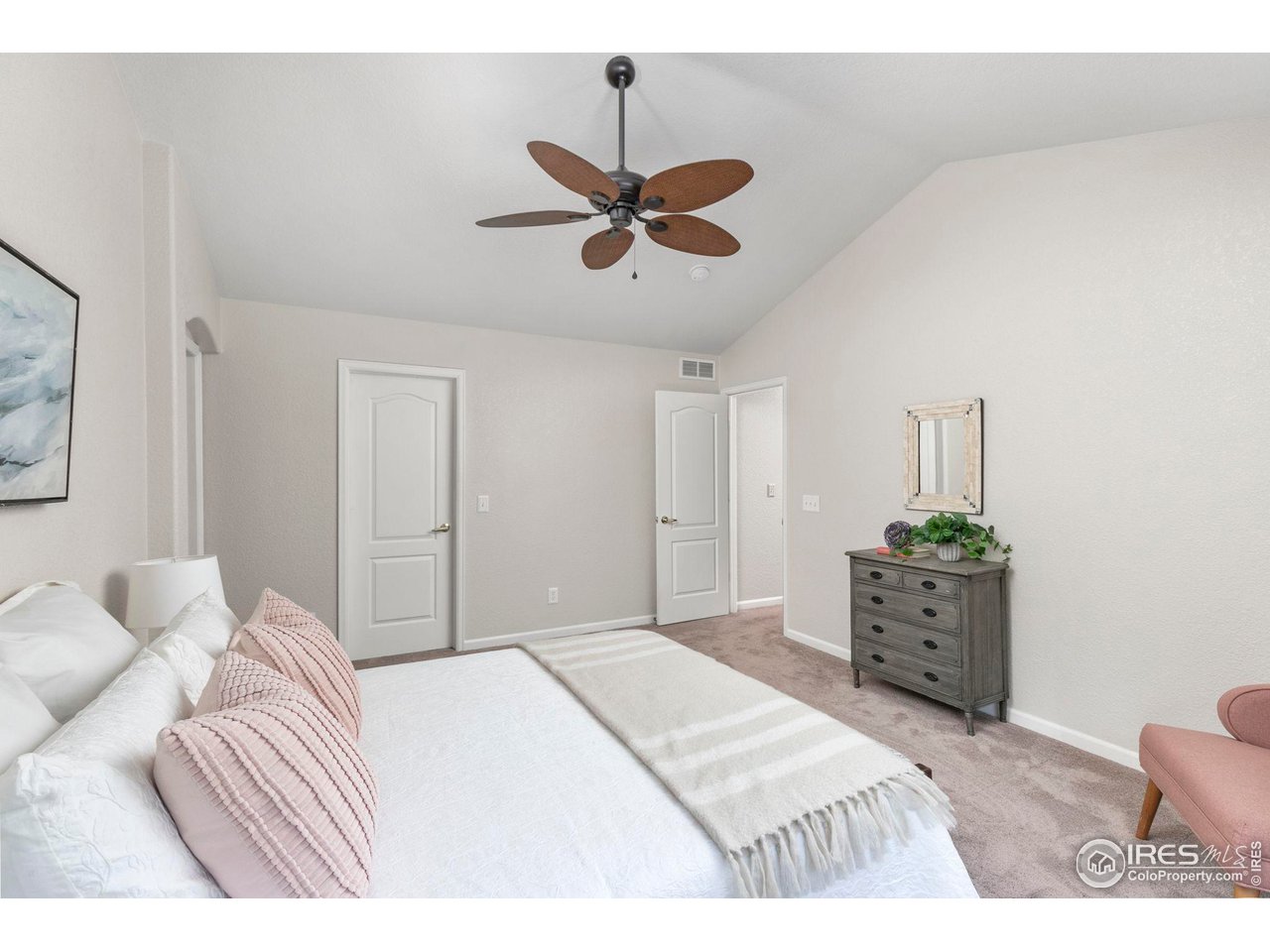 Furnished bedroom with a white bed, blush pillows, wood-bladed ceiling fan, and gray dresser.
