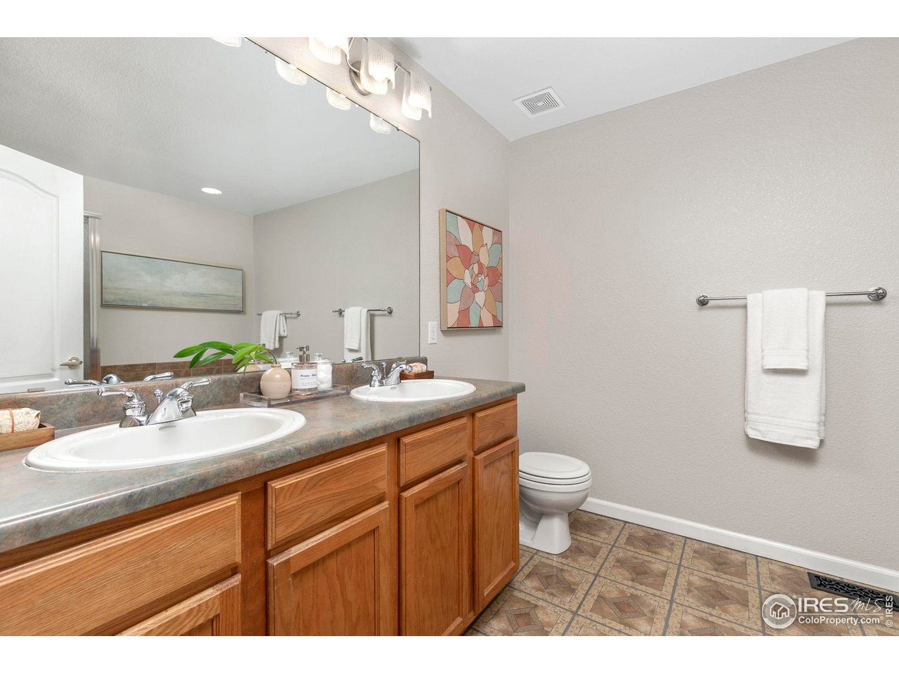 Bathroom with a double-sink wood vanity, large mirror, and patterned tile floor.