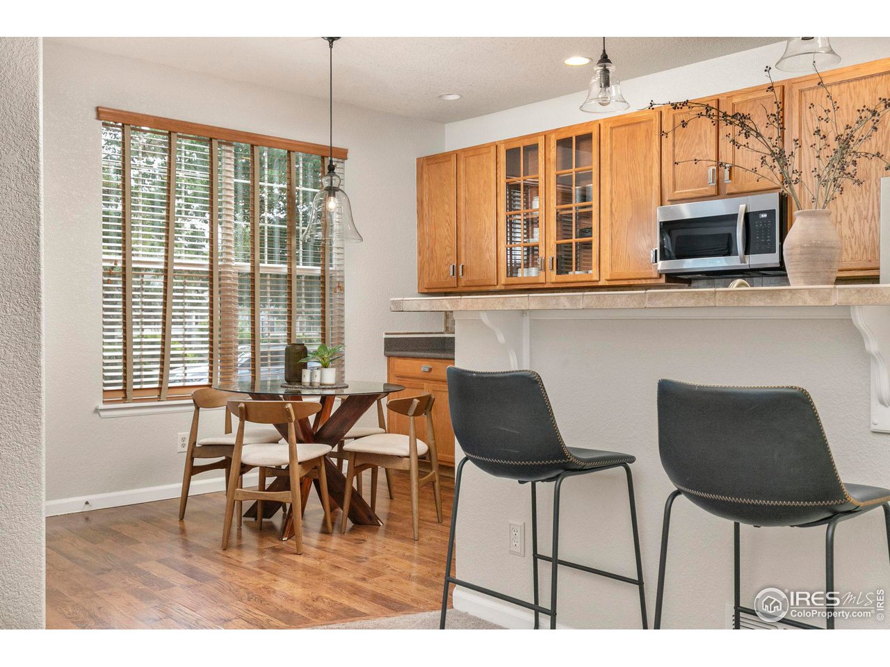 Kitchen and dining area with wood cabinetry, breakfast bar stools, and a round table beside a large window.