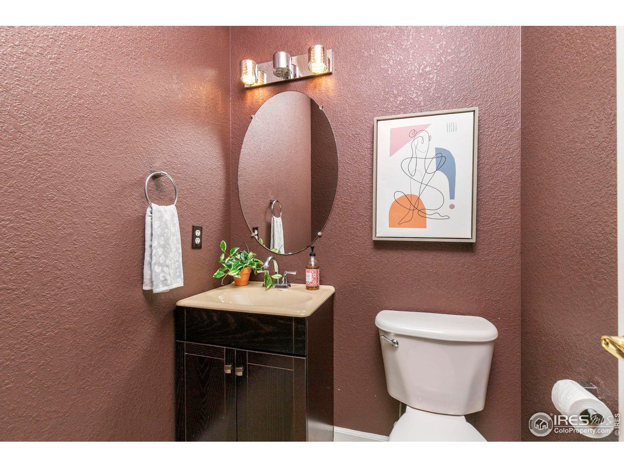 Bathroom with a dark wood vanity, oval mirror, and textured mauve walls.