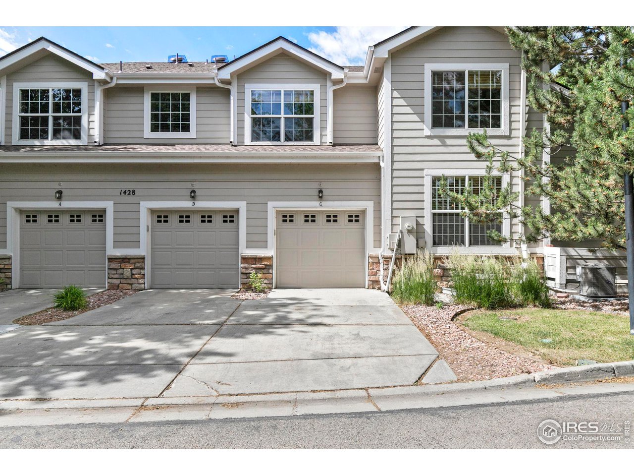 Gray two-story attached home with three garage doors, stone accents, and a broad concrete driveway.