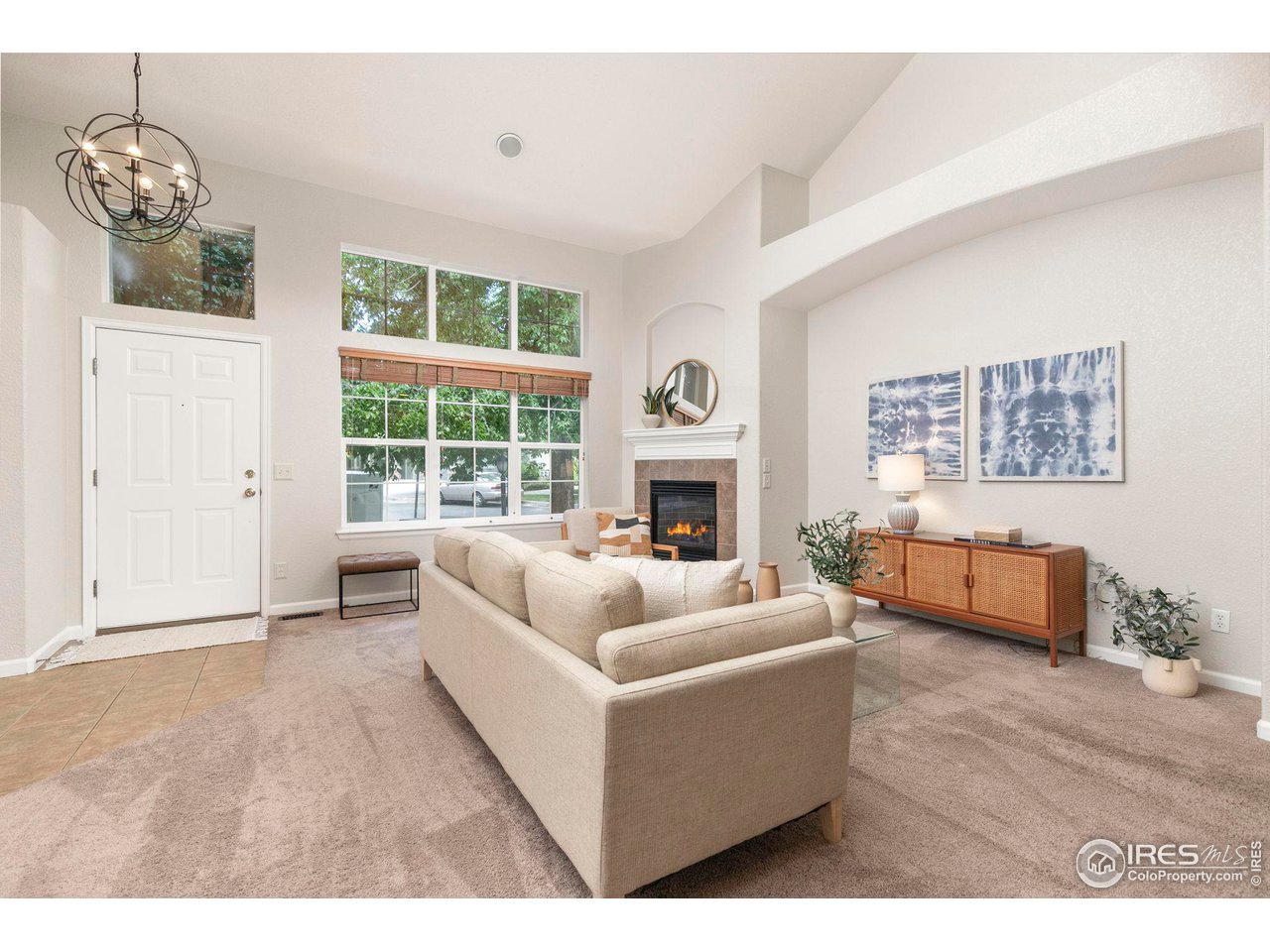 Staged living room with a beige sofa, tall windows, and a lit fireplace.