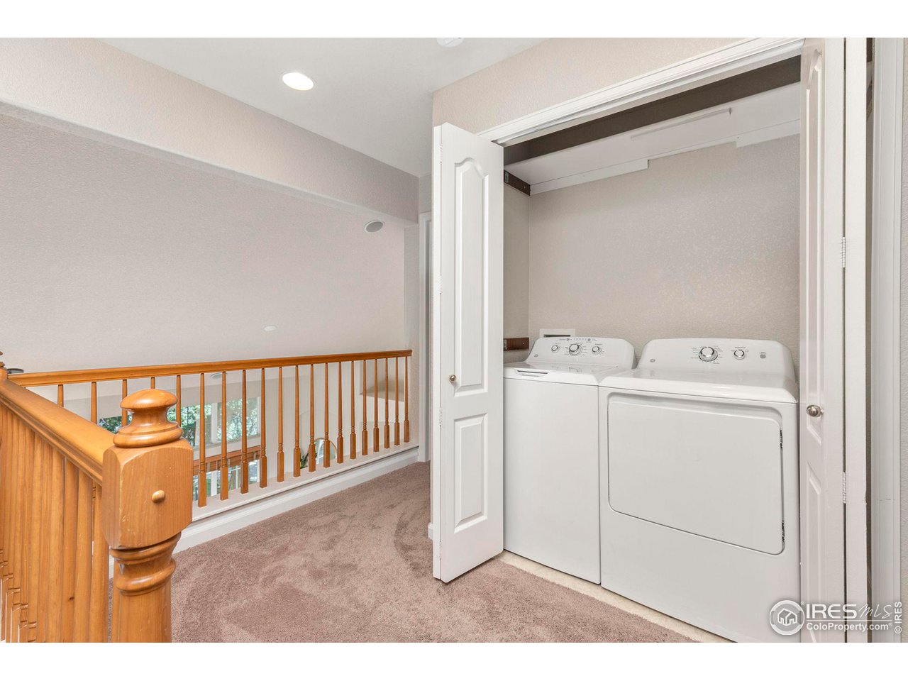 Washer and dryer in an open laundry closet beside a carpeted landing with a wooden railing.