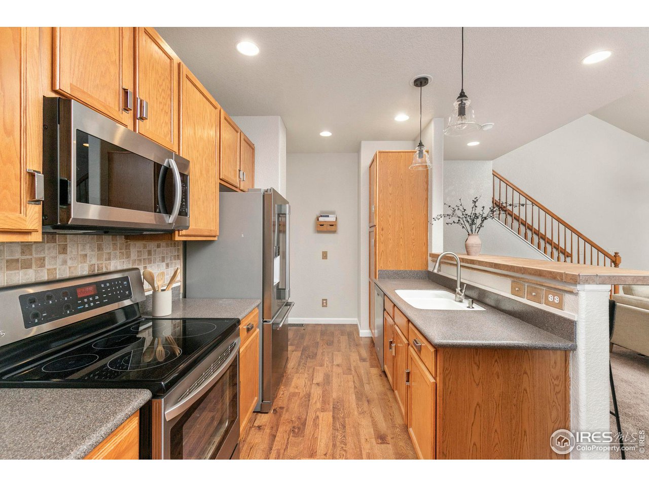 Kitchen with honey-colored cabinets, stainless steel appliances, and a long countertop beside the staircase.