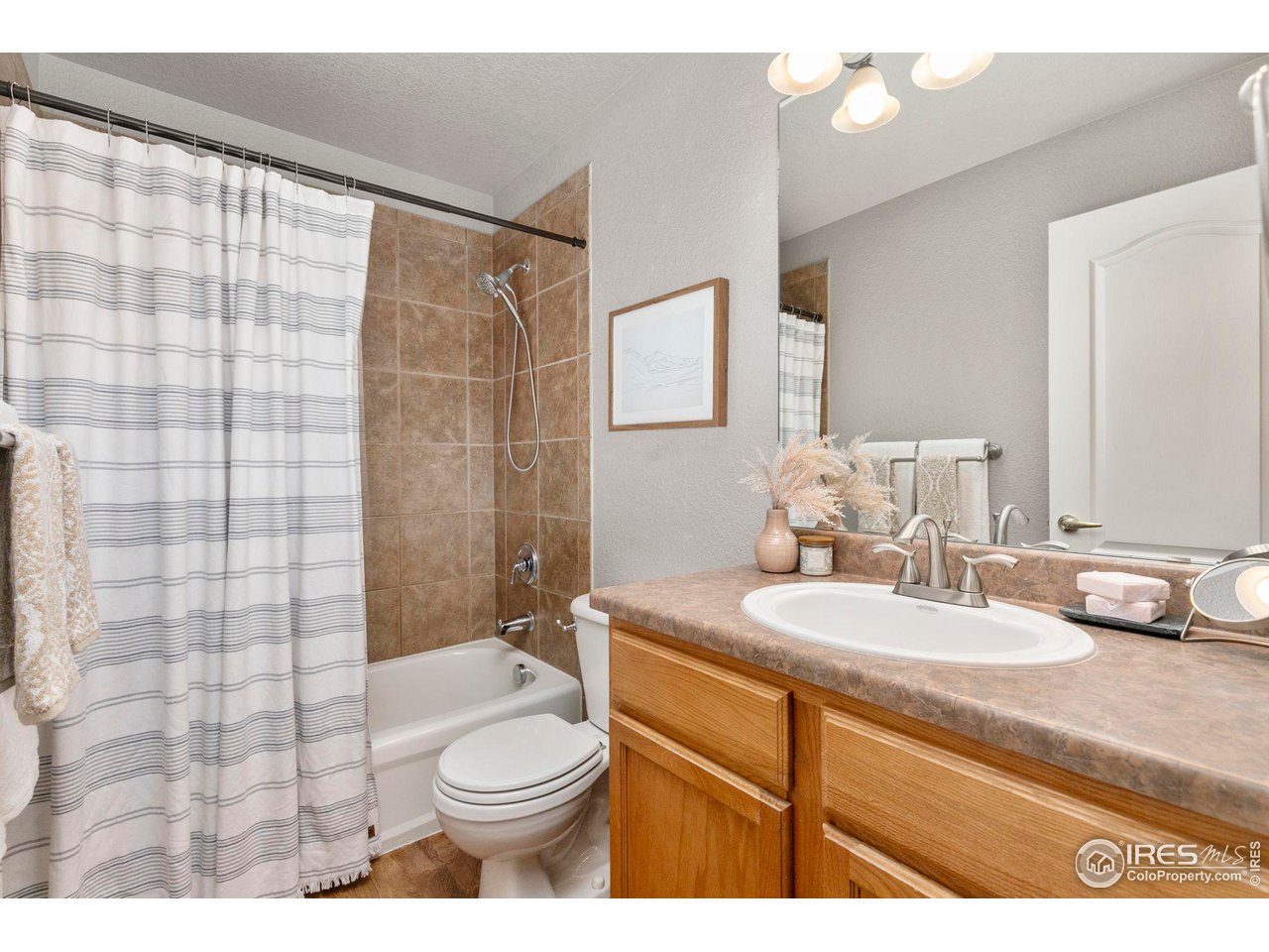 Bathroom with a striped shower curtain, brown tile, and a wood vanity with a large mirror.