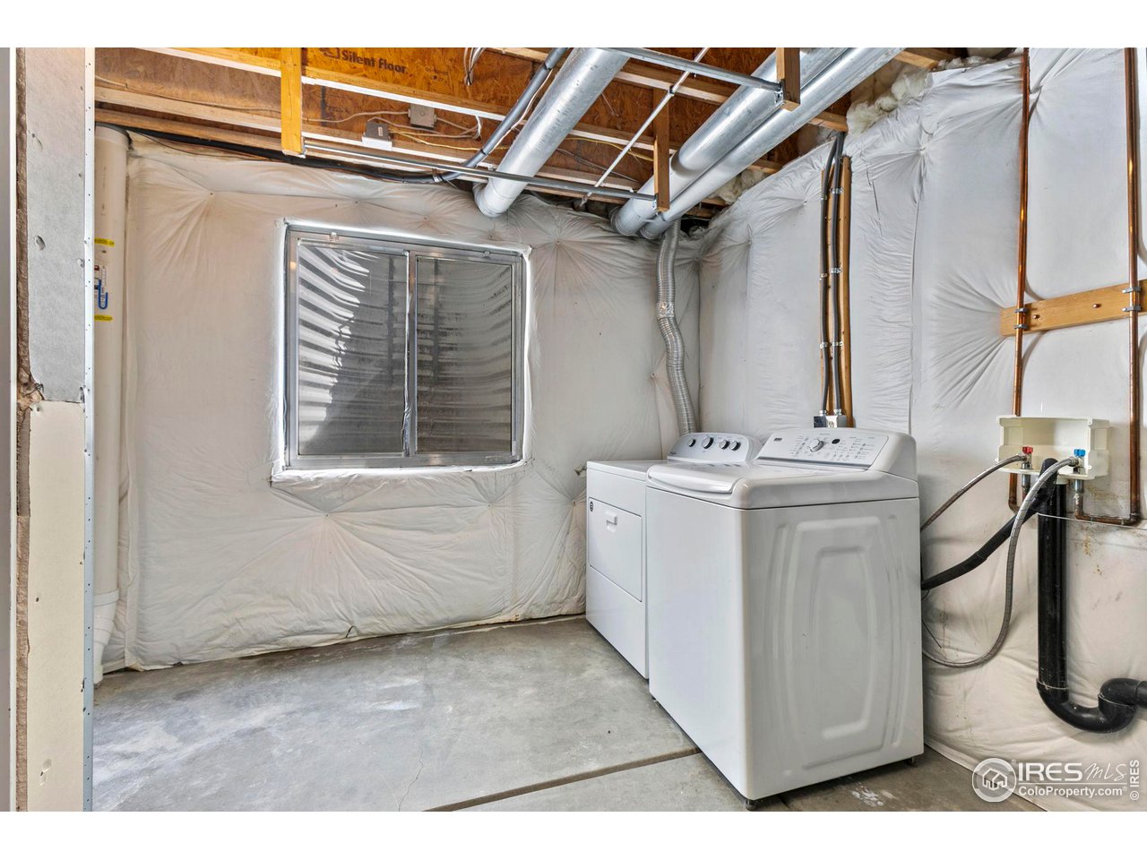 Basement laundry area with a washer and dryer beneath exposed ductwork.