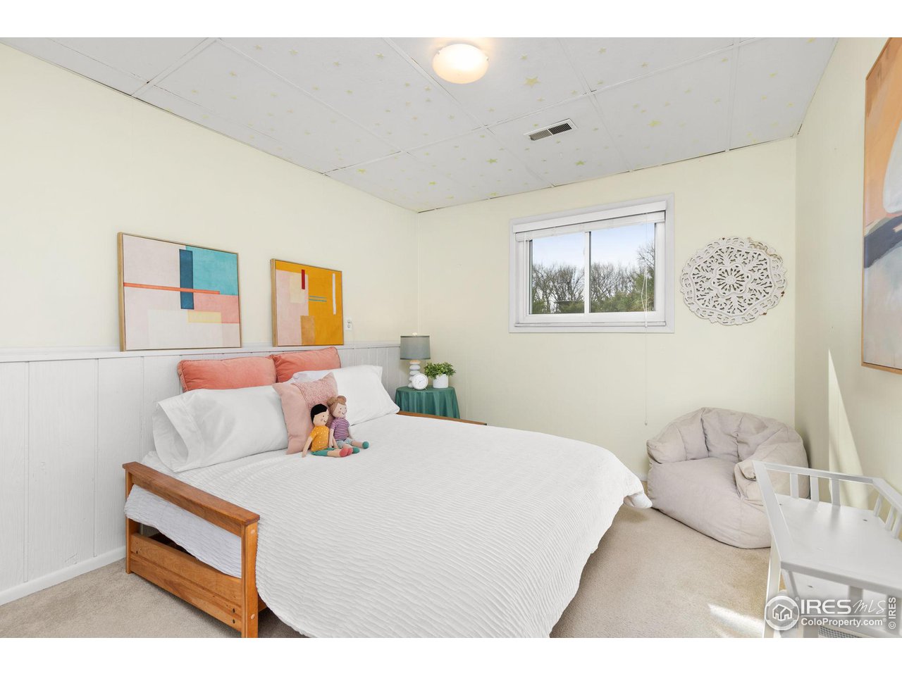 Bedroom with a white bed, coral pillows, colorful abstract artwork, and a window.
