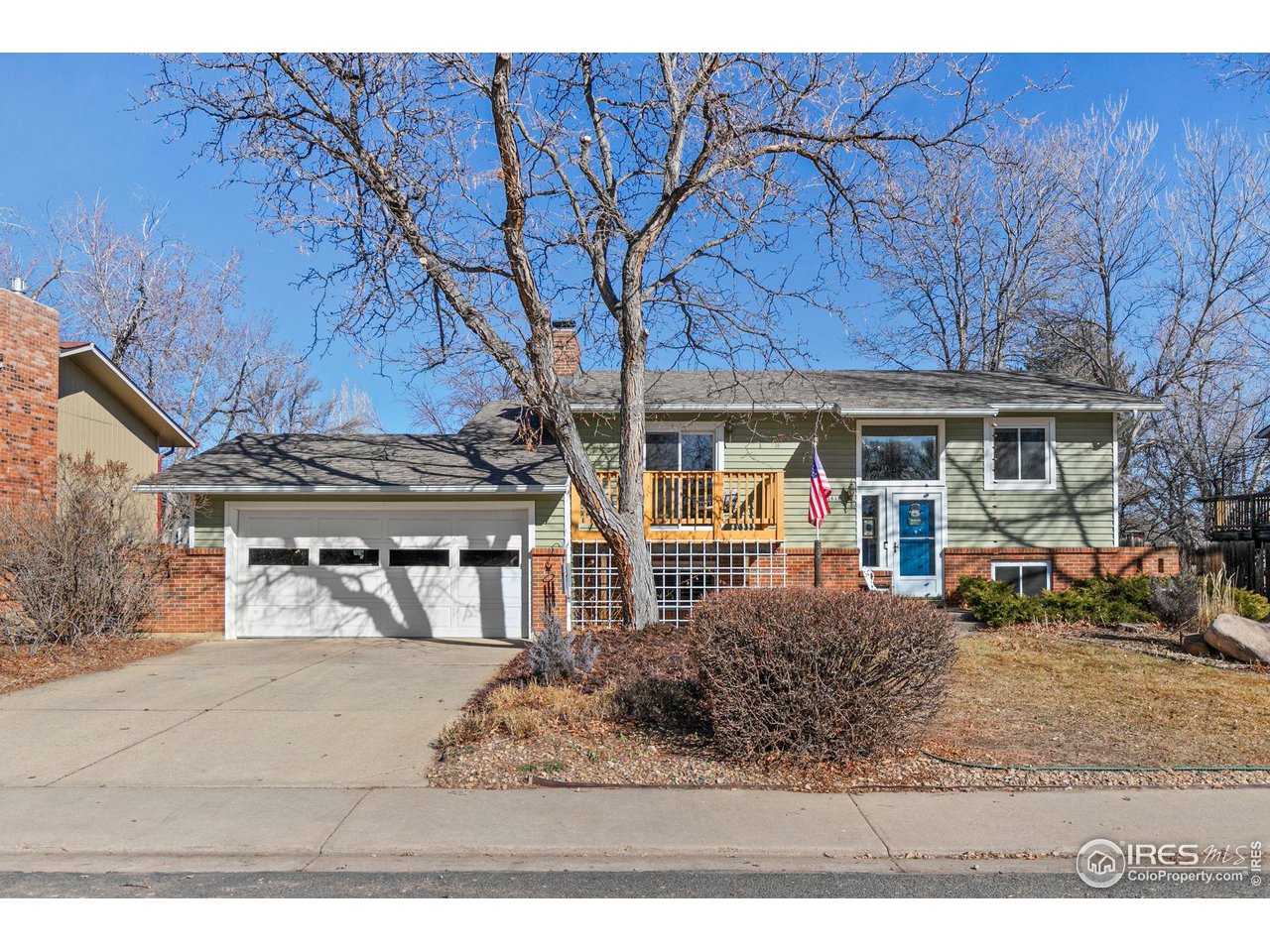 Split-level home with a blue front door, brick accents, attached garage, and leafless trees.