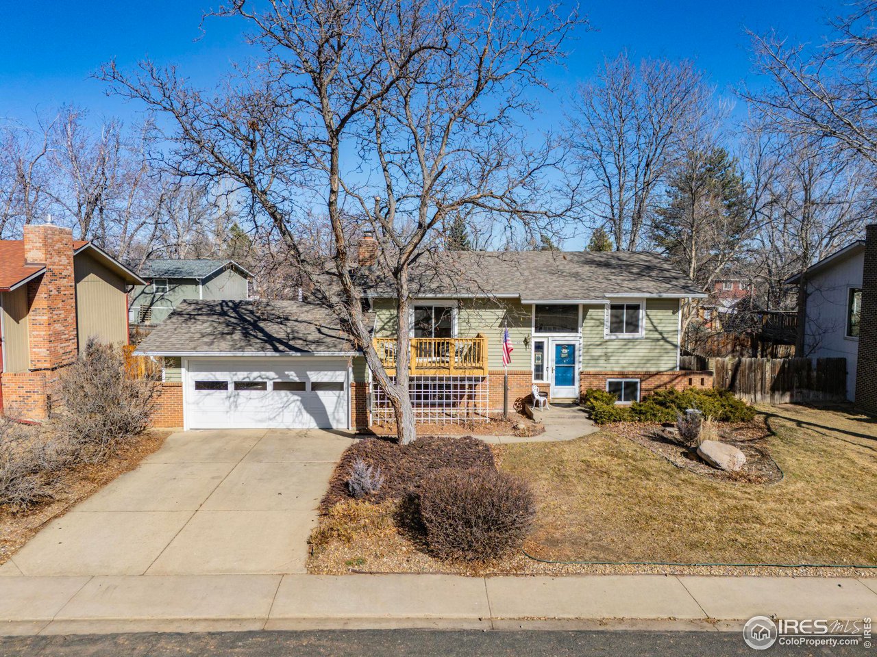 Green split-level home with brick accents, attached garage, and a large leafless tree in the front yard.