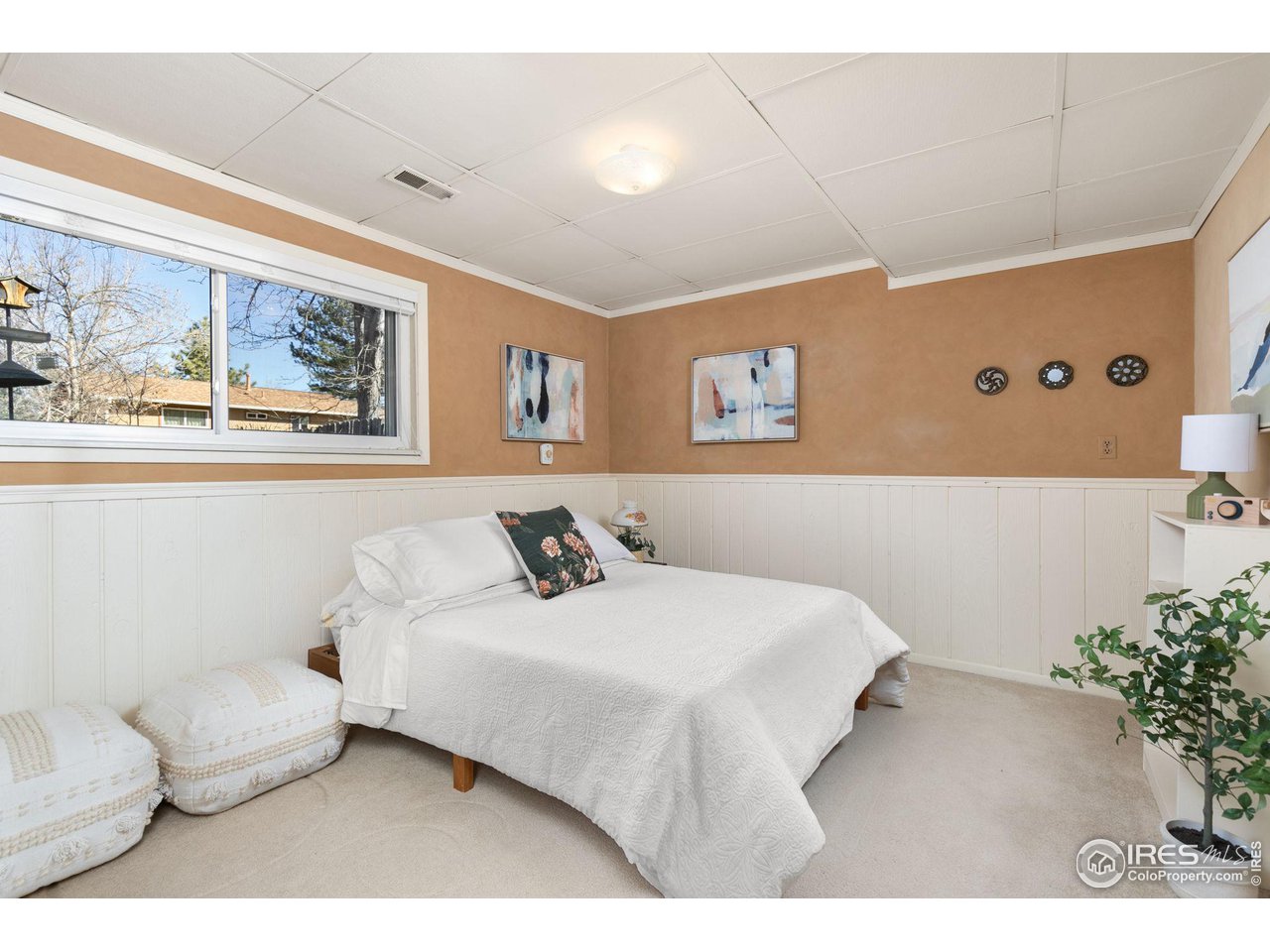 Bedroom with a white bed, peach walls, and a wide window overlooking trees.