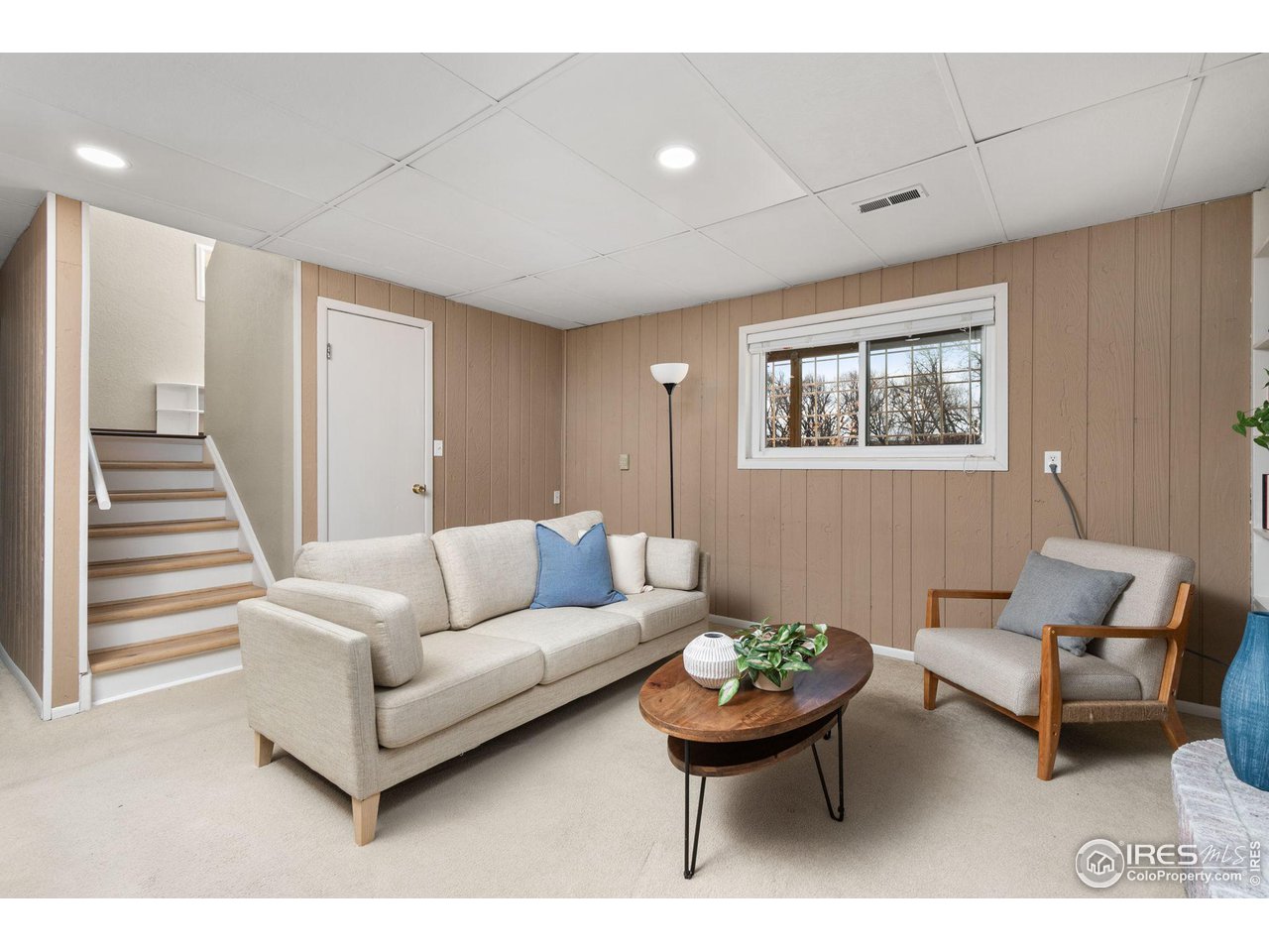 Living room with cream seating, paneled walls, a wood coffee table, and stairs beside the sofa.