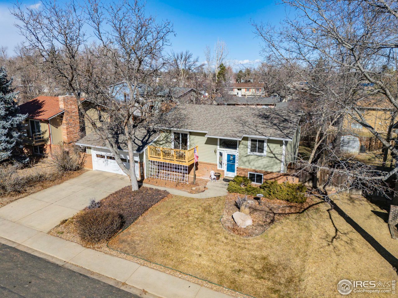 Aerial view of a single-story green-and-brick home with an attached garage and small wooden deck.