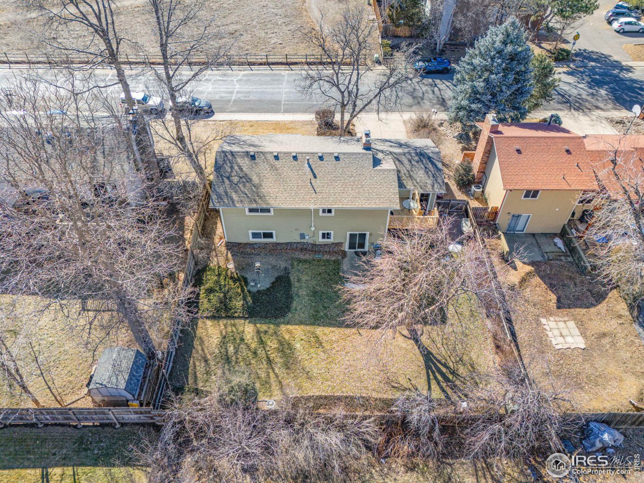 Aerial view of the home's fenced backyard and rear exterior, bordered by leafless trees.