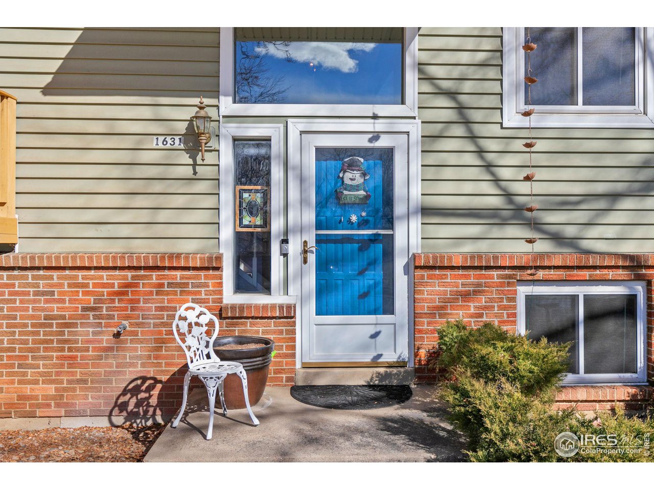 Home’s front entrance with a white-framed glass door, brick facade, and small patio chair.