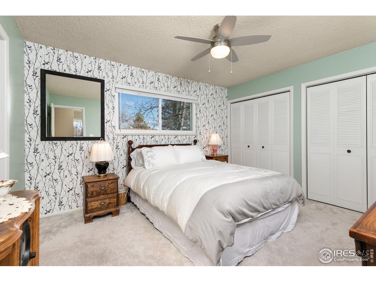 Bedroom with a white bed, branch-pattern wallpaper, pale green walls, and white closet doors.