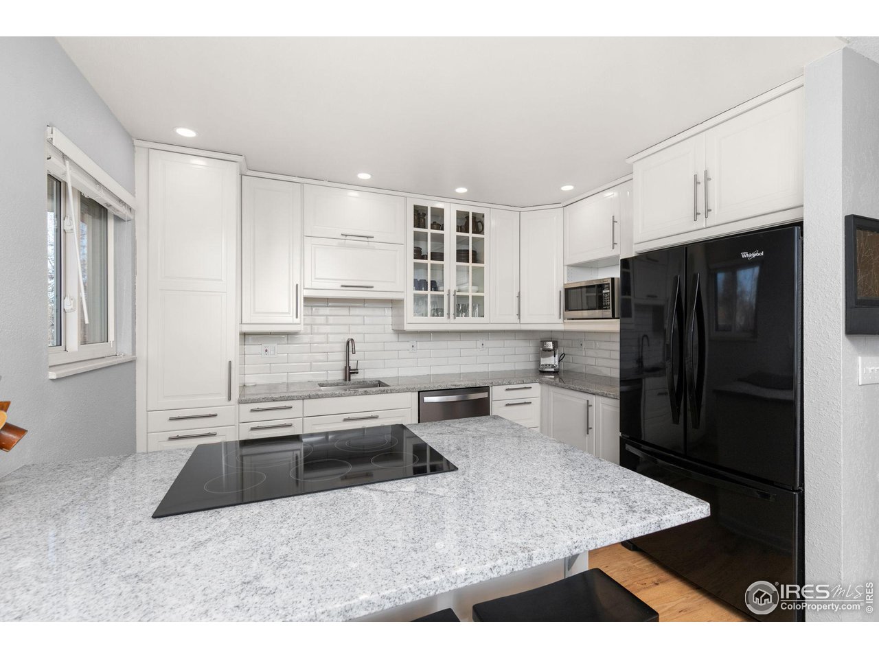 Kitchen with white cabinets, granite island and cooktop, subway tile backsplash, and black appliances.