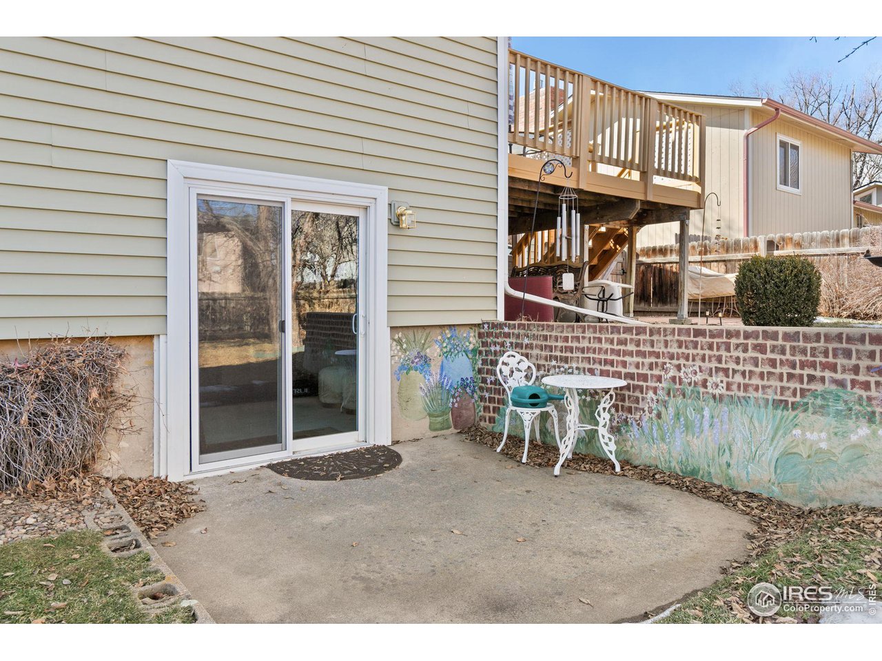 Rear patio with a white table and chairs beside a painted brick wall, beneath a raised wooden deck.