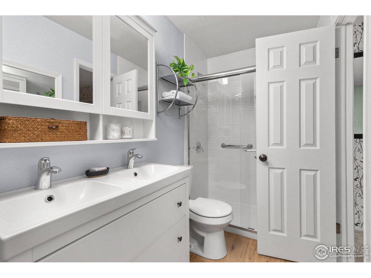 Bathroom with a double-sink vanity, mirrored cabinets, and a tiled shower with grab bars.