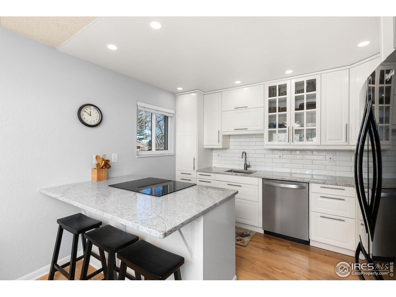 Renovated kitchen with white cabinets, granite island, black stools, and stainless-steel appliances.