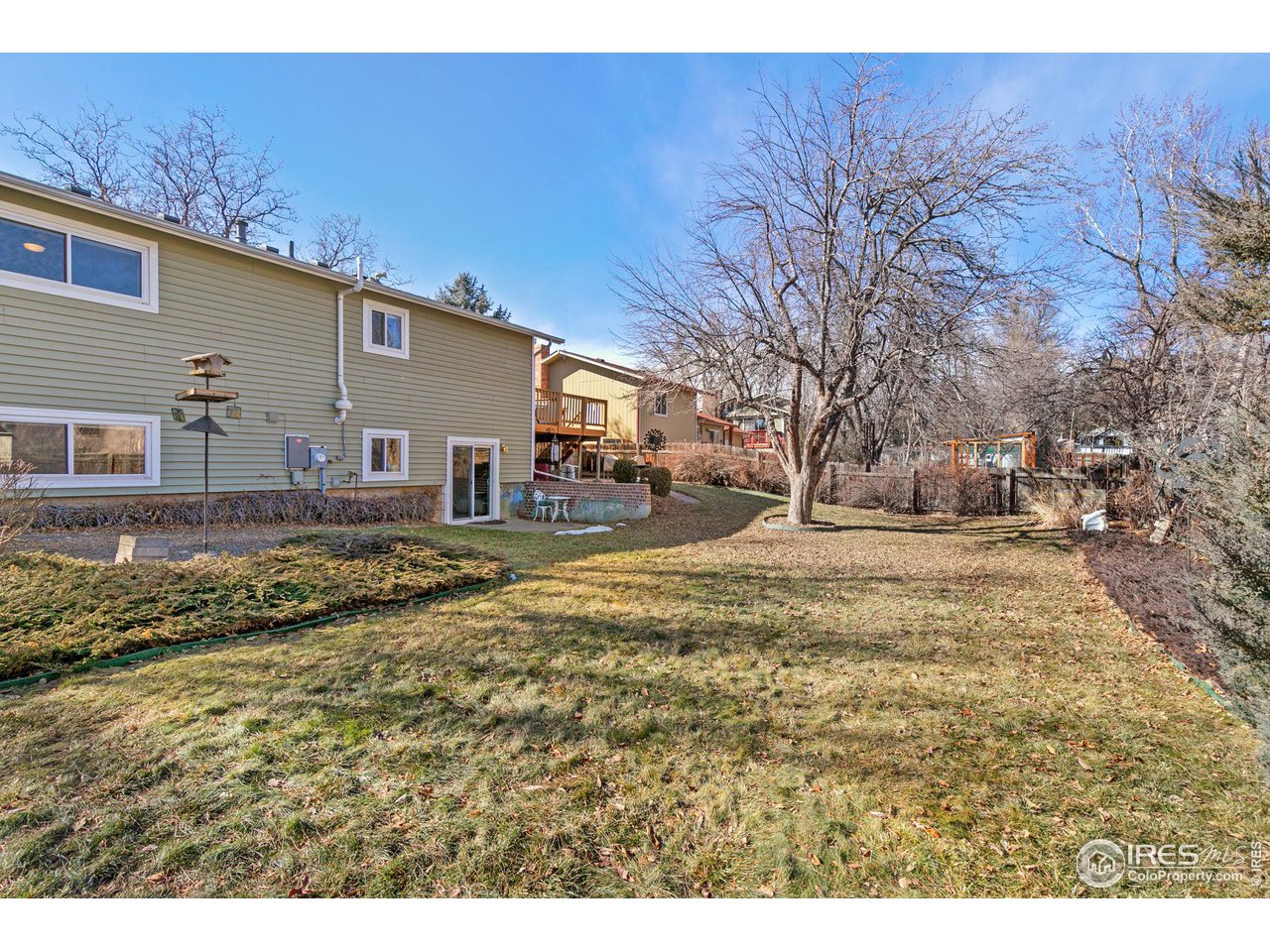 Home’s rear exterior and broad grassy yard with leafless trees and a fenced play area.