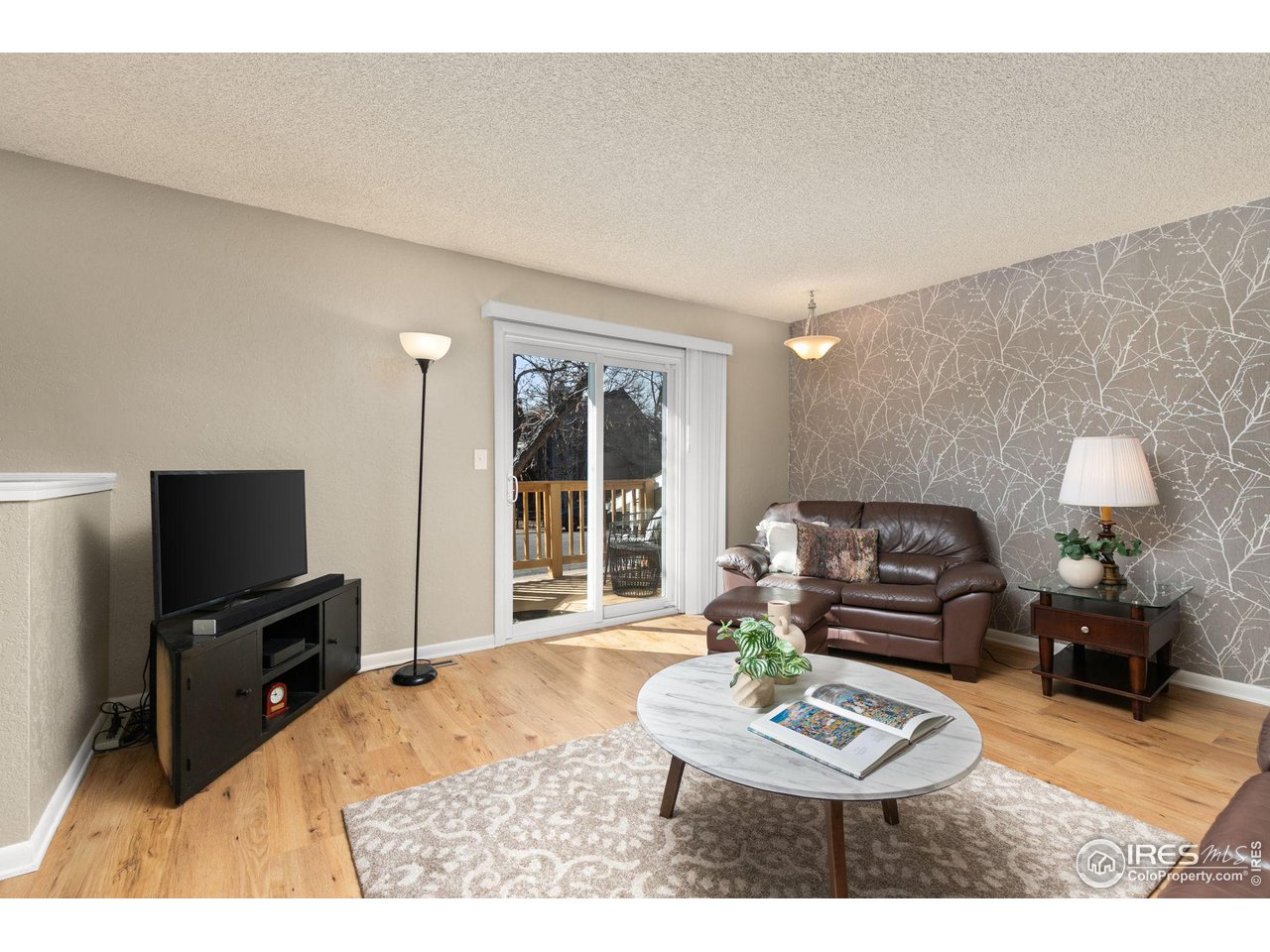 Living room with brown leather sofa, branch-pattern accent wall, and sliding doors to a deck.