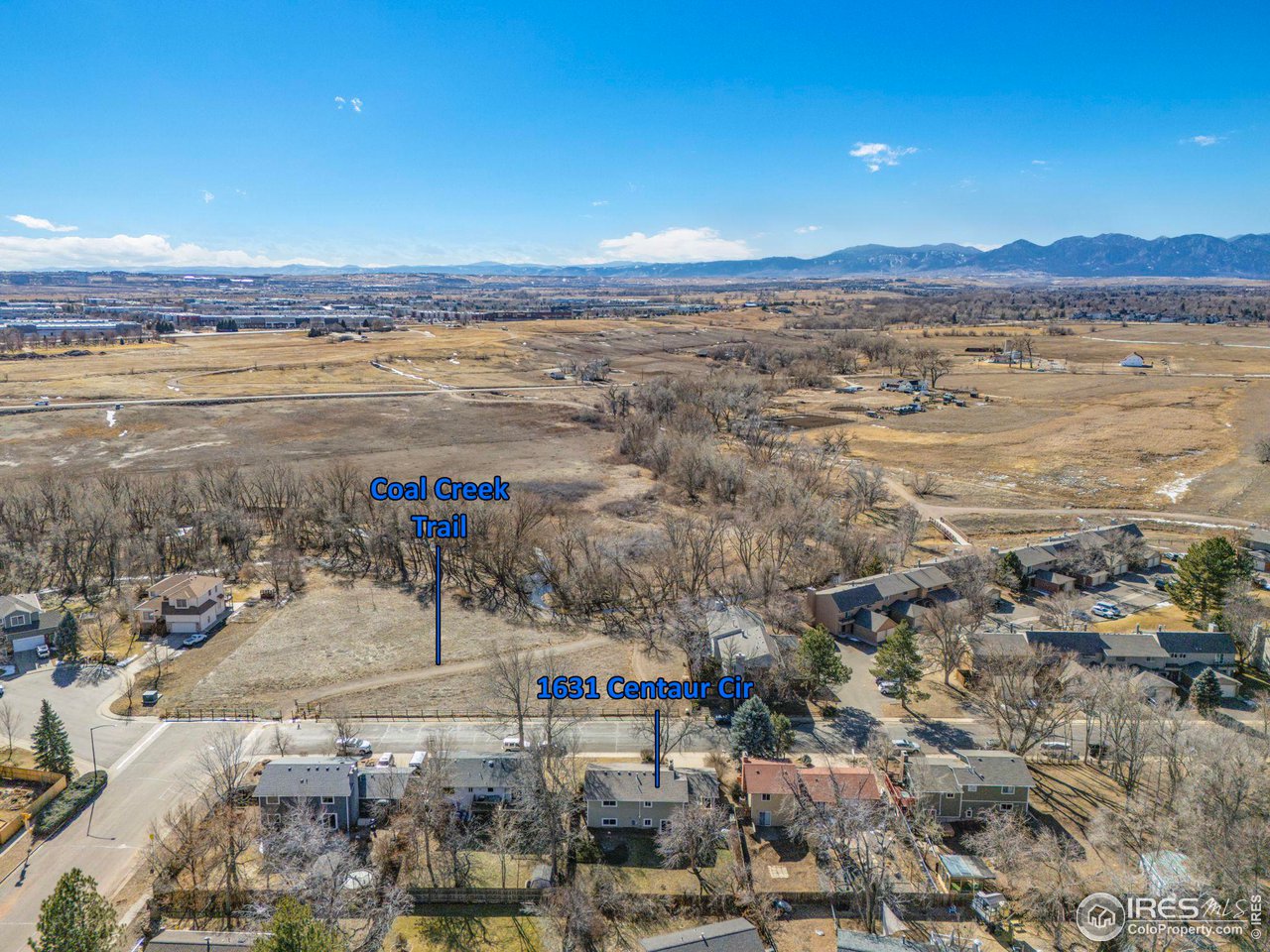 Aerial view of 1631 Centaur Cir, with Coal Creek Trail, open fields, and mountains beyond.