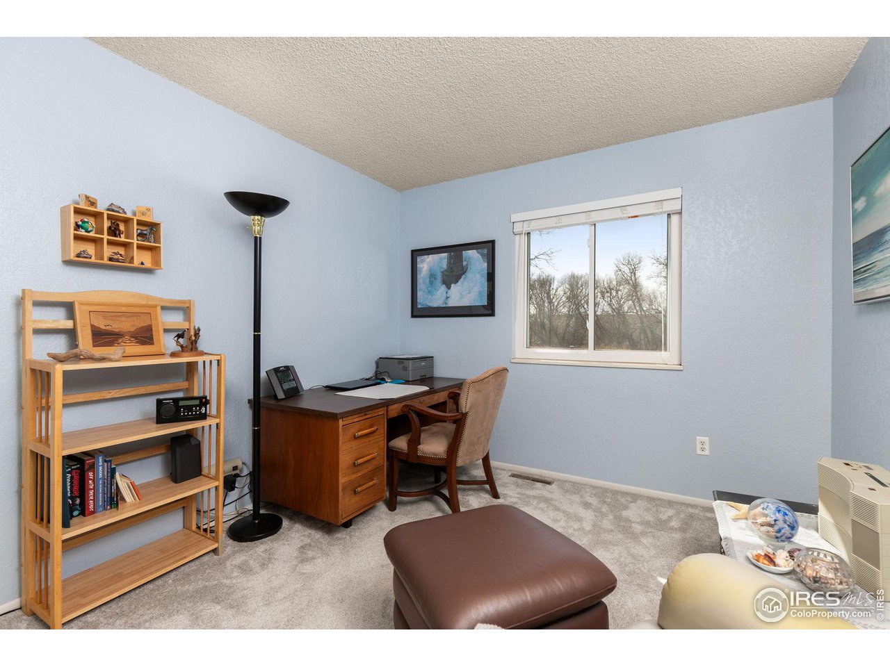 Furnished home office with a wooden desk and shelving beside a window overlooking leafless trees.