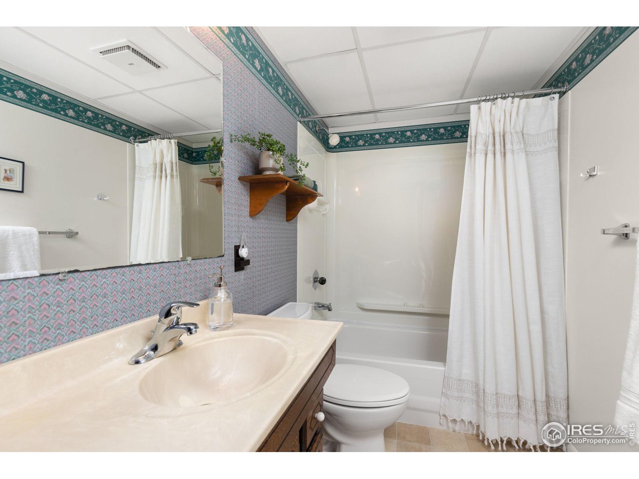 Bathroom with a cream vanity, large mirror, patterned wallpaper, and a tub behind a white curtain.